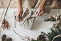 Plastic free holidays, zero waste Christmas. Hands wrapping christmas gift in linen fabric in furoshiki style on white rustic