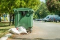 Plastic green garbage cans on the street in the city with junk bags full of litter on the asphalt road