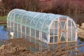 Plastic greenhouse with wooden doors surrounded with rising floodwater