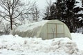 Plastic greenhouse with wooden doors surrounded with snow
