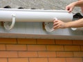 Contractor installing plastic roof gutter. Plastic Guttering Replace, Rain Guttering & Drainage Repair by Handyman hands.