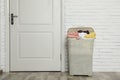 Plastic laundry basket full of dirty clothes near brick wall in room Royalty Free Stock Photo