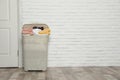 Plastic laundry basket full of dirty clothes near brick wall in room Royalty Free Stock Photo