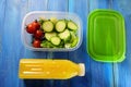 Plastic lunch box with fresh cucumber salad and cherry tomatoes on blue wooden table. Nearby is plastic bottle of orange juice and Royalty Free Stock Photo