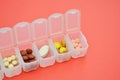 Plastic daily organizer for pills, box with different pills on coral background with copyspace Royalty Free Stock Photo