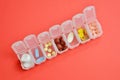 Plastic daily organizer for pills, box with different pills on coral background with copyspace, top view Royalty Free Stock Photo