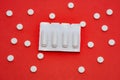 Plastic packaging with vaginal or rectal suppositories is on redbackground surrounded by round tablets that form ornament in polka