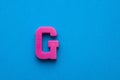 Alphabet letter G - Pink plastic piece on blue foamy background