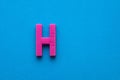 Plastic pink letter H uppercase on blue foamy background