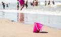 Plastic pink toy bucket left alone on the beach sand near water, blurred people on background - concept of vacation safety, drowni Royalty Free Stock Photo