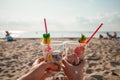 Plastic pollution in ocean environmental problem, girls hands holding plastic cups with straws and cocktail from beach garbage -