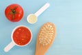Plastic scoops with tomato puree, olive oil and wooder hair brush. Ingredients for preparing homemade hair mask. DIY cosmetics.