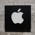 Plastic sign of a white apple on a black background on a travertine wall, logo of the American computer company Apple