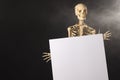 Plastic skeleton holding paper sheet and smoke with copy space on black background