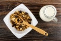 Spoon in bowl with cereal breakfast with peanut and raisin, pitcher with yogurt on wooden table. Top view