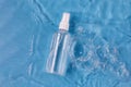 Plastic spray bottle of cosmetic product and splashing water on blue background Royalty Free Stock Photo