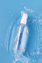 Plastic spray bottle of cosmetic product and splashing water on blue background Royalty Free Stock Photo