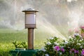 Plastic sprinkler irrigating flower bed on grass lawn with water in summer garden. Watering green vegetation duging dry season for Royalty Free Stock Photo