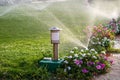 Plastic sprinkler irrigating flower bed on grass lawn with water in summer garden. Watering green vegetation duging dry season for Royalty Free Stock Photo