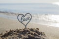 Plastic stick in shape of heart and word Love in sand on beach seashore