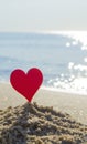 Plastic stick in shape of red heart in sand on sandy beach of sea shore