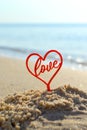 Plastic stick in shape of red heart and word Love in sand on beach seashore