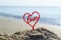 Plastic stick in shape of red heart and word Love in sand on beach seashore Royalty Free Stock Photo