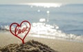 Plastic stick in shape of red heart and word Love in sand on beach seashore Royalty Free Stock Photo