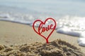 Plastic stick in shape of red heart and word Love in sand on beach seashore Royalty Free Stock Photo