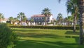 Plastic sun loungers and umbrellas are set up on a tiled area by the pool, behind which stands the building. Ornamental shrubs and Royalty Free Stock Photo