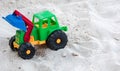 A Plastic Toy Bulldozer Color Green, Red, Yellow And Blue With Black Big Wheels Placed On A White Sand In A Beach Resort