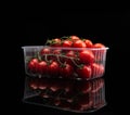 Cherry tomatoes in a plastic container. Group of small tomatoes on twigs, on black background, with visible reflection.