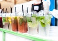 Plastic transparent glasses with different kinds of cold lemonade stays on white table with green border on blurry beach bar