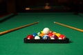 Plastic triangle rack with billiard balls and cues on green table indoors Royalty Free Stock Photo
