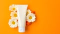 a plastic tube of cream set against an orange background adorned with vibrant gerbera flowers. Royalty Free Stock Photo