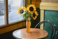 a plastic vase with faux sunflowers on a small bistro table in a caf corner