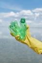 Plastic waste pollution. Vertical shot of a volunteer wearing yellow rubbish glove holding used plastic bottle against