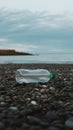 Plastic Water Bottle on Dark Pebble Beach with Blurred Ocean and Cloudy Sky in Background Royalty Free Stock Photo