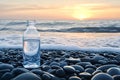 Plastic water bottle on pebble beach at sunset reflecting ocean and sky Royalty Free Stock Photo