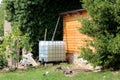 Plastic water tank with metal support connected to house roof gutter with metal pipe for storing rainwater and later use in