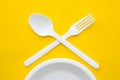 Plastic white crossed fork, spoon and plate on yellow background. Cooking utensil. Cutlery sign. Top view. Minimalist Style. Copy Royalty Free Stock Photo