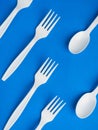 Plastic white disposable fork and spoon on a trendy blue color background. Concept plastic dishes, fast food, plastic pollution. Royalty Free Stock Photo