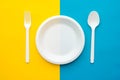 Plastic white fork, spoon and plate on yellow and blue background. Cooking utensil. Top view. Minimalist Style. Copy, empty space Royalty Free Stock Photo