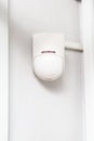 Plastic white infrared motion sensor with a red light bulb on a white wall close-up. Vertical orientation. Royalty Free Stock Photo