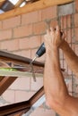 Plastic window installation. Worker attaches anchor plate with screwdriver.