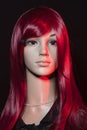 Mannequin with bright long red hair posing on a black background