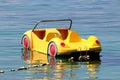Plastic yellow paddle boat in shape of car floating on calm sea tied to shore with strong rope and multiple small white buoys
