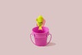 A plastic yellow and pink fish jumping out of a pink bucket against sandy background. Minimal surreal funny concept for summer