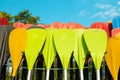 Plastic yellow red colored paddles for paddle board SUP in storage on the beach against a sky background