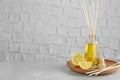 Plate with aromatic reed freshener and lemon on table against textured wall